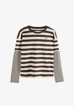 Person with long blond hair wearing oversized black sunglasses, a layered black and white striped shirt, loose black pants, and yellow sneakers.