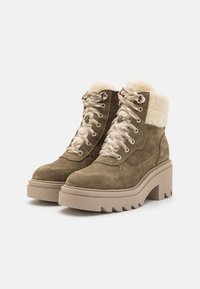 Bottines en daim marron avec un revers en fausse fourrure, des œillets en métal et une semelle compensée beige épaisse. Présente des lacets beiges et un profil de semelle prononcé.