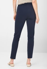 Marineblaue Slim-Fit-Hosen mit einem strukturierten Bund, aus weichem, elastischem Material gefertigt, mit einem sauberen Saum und Knöchellänge. Flache Gesäßtaschen sichtbar.