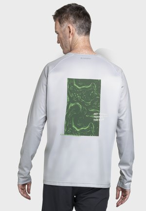 Mann trägt ein hellgraues Langarmshirt mit einem grünen abstrakten Design und dem Text "Hey Nature, danke für die Fahrt" auf der Rückseite.