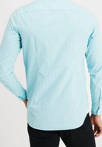 Ljusblå rutig skjorta med lång ärm, rak skärning och knäppningar vid ärmsluten. Mjuk tyg och slät textur, med en klassisk krage.