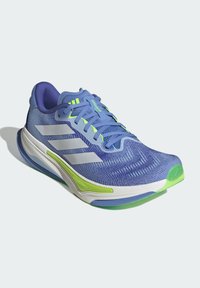 Blue athletic shoe made of mesh material with white and lime green accents. Features textured design, prominent stripes, and a rounded toe.