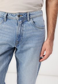 Světle modré džíny z denimu s klasickým střihem, pěti kapsami, zapínáním na knoflíky a jemným vyblednutím látky.