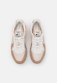 Světlé béžové a bílé tenisky z prodyšné síťoviny a semiše, s kulatou špičkou, zavazováním na tkaničky a logem značky na jazyku.