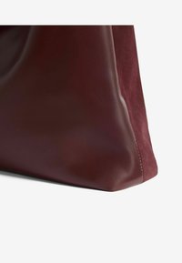 Bordo kožni ručni predmet s glatkom, sjajnom završnom obradom; uključuje mekani suedin panel i strukturirani donji kut.