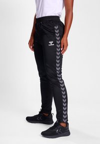 Zwarte sportieve broek met een gestructureerd visgraatpatroon aan de zijkant. Gemaakt van een zachte stof, met een elastische tailleband en een merkaccent.