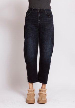 Person wearing black cropped jeans and beige fuzzy ankle boots standing against a plain white background.