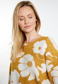 Maglione lavorato a maglia con motivo floreale giallo e bianco, con scollo ampio e una texture morbida. Design a maniche lunghe con un aspetto accogliente.