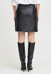 Schwarzer Leder-Minirock mit sleekem Design, der eine figurbetonte Silhouette und subtile Nähte aufweist. Kombiniert mit hohen schwarzen Stiefeln.
