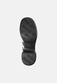 Schwarze Gummisohle mit erhabenem "Camper"-Logo, flachem Design und einer Größenmarkierung von 38. Leicht gewölbte Konturen für zusätzlichen Komfort.