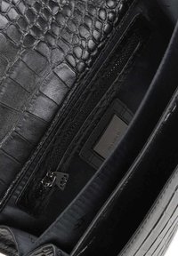Czarna skórzana torebka z fakturowanym wzorem krokodyla, wewnętrzną kieszonką zamykaną na zamek i gładkim materiałowym wykończeniem. Minimalne logo widoczne.