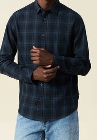 Mörkblå rutigt skjorta med knappar och slim fit, med krage, långa ärmar och en slät tygstruktur. Blå och svarta rutor synliga.