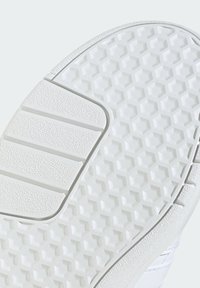 Semelle blanche de sneaker avec motif de bande de roulement hexagonal et grip rectangulaire texturé près du talon pour traction et durabilité.