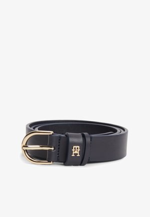 Curea din piele bleumarin cu cataramă rotundă aurie și logo mic auriu pe bucla curelei, rulată pe un fundal alb.