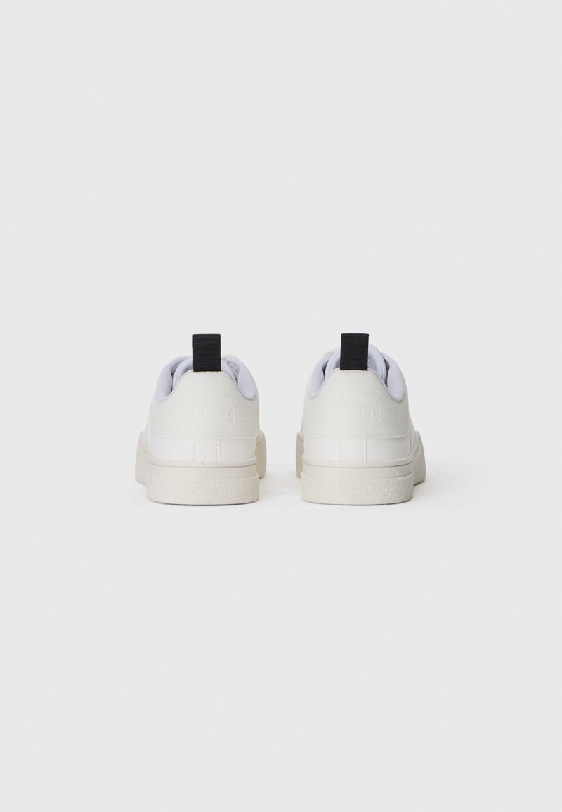 Zapatillas blancas con parte superior de cuero suave, punta redonda y suela de goma. En la parte posterior cuenta con un tirador negro. Diseño minimalista con líneas limpias.