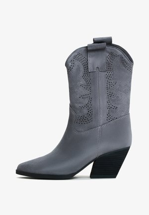 Stivale cowboy in ecopelle grigia con punta appuntita, ritagli decorativi e tacco impilato. Presenta un manico per facilitarne l'indossamento.