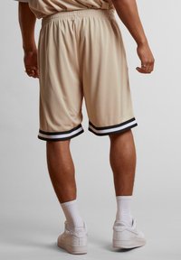 Shorts de sport beiges en tissu léger, avec un ourlet à rayures noires et blanches, dotés d'une taille élastique pour un meilleur confort.