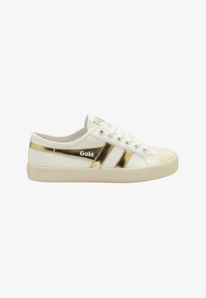 Sneaker Gola bianca low-top con suola beige, con strisce dorate metalliche e logo del marchio sul lato.
