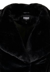 Gros plan d'un col de manteau en fausse fourrure noire montrant l'étiquette de la marque Urban Classics et la taille XS à l'intérieur de l'encolure.