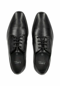 Zapatos de cuero negro con una textura suave y detalles perforados en la zona de los dedos. Presentan un diseño de cordones y una forma minimalista.