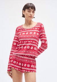 Rdeč komplet pižame z vzorcem, ki vključuje majico z dolgimi rokavi in hlačke, z belim cvetličnim in jelenčkovim motivom, izdelan iz mehke, udobne tkanine.