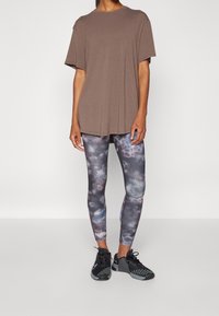 Camiseta marrón oversized, combinada con leggings ajustados con un estampado de galaxia multicolor. Zapatillas deportivas negras con detalles texturizados.