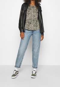 Chaqueta de cuero negra, camisa a rayas verde y crema, vaqueros rectos de color azul claro y zapatillas verde oliva con detalles en blanco.