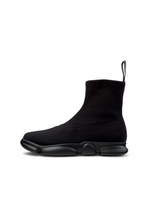 Bottines en tricot noir avec une semelle en caoutchouc cylindrique, présentant une texture lisse et une languette à l'arrière pour un enfilage facile.