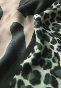 Stof met een mix van abstracte zwarte vormen op een beige achtergrond en een groene luipaardprint. Zachte, gladde textuur met gelaagde plooien.