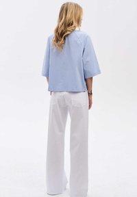 Jasnoniebieska, luźno dopasowana bluzka z szerokimi rękawami, w połączeniu z białymi, wysokim stanem, szerokimi spodniami. Gładka bawełniana faktura, minimalistyczny design.