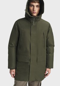 Parka vert olive en matériau résistant à l'eau. Comprend une capuche, deux poches à rabat, une fermeture éclair à l'avant et une coupe droite.
