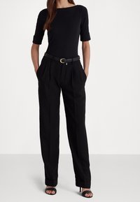 Svart figursydd topp med korta uppvikta ärmar, kombinerad med högmidjade svarta byxor med veck, accentuerad av ett smalt svart bälte med ett guldspänne.