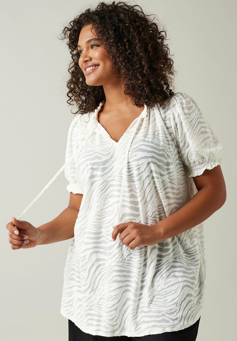Weiße Bluse mit einem strukturierten Zebra-Streifenmuster, kurzen Puffärmeln, V-Ausschnitt und verstellbarem Bindegürtel am Ausschnitt.