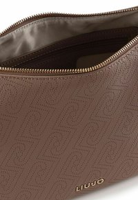 Borsa in pelle marrone con motivo in rilievo e cerniera color oro. L'interno è foderato con un tessuto beige liscio, con una tasca con zip.