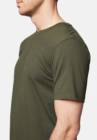 Koszulka z krótkim rękawem w kolorze oliwkowym, wykonana z miękkiej bawełny. Posiada okrągły dekolt oraz dopasowany krój z gładką teksturą.