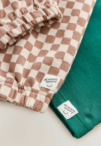 To stykker stofprøver: den ene i beige med et brunt ternet mønster, den anden helt grøn. Hver har et mærke med teksten "ALWAYS HAPPY."