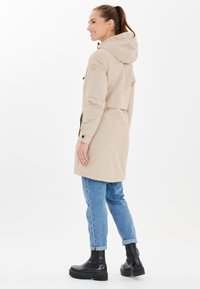 Vaalea takki, jossa on huppu, istuva vyötärö, sivutaskut ja nappikiinnitys hihasuissa. Päällä vaaleansiniset farkut ja mustat nilkkurit.