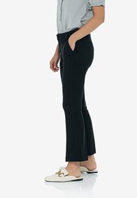 Czarne spodnie o dopasowanym kroju z bocznymi kieszeniami, zestawione z białymi butami wsuwanymi z złotymi akcentami.