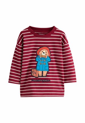 Červeně pruhovaná košile s dlouhým rukávem, která zobrazuje ilustraci medvídka Paddingtona, jak drží sendvič, s modrými akcenty a výšivkou.