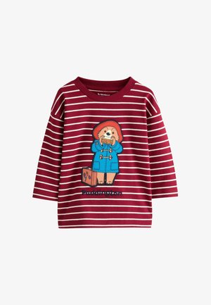 Rdeče prugasta dolga srajca z dolgimi rokavi, ki prikazuje ilustracijo medvedka Paddingtona, ki drži sendvič, s plavimi dodatki in vezeninami.