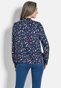 Marineblauwe blouse met een kleurrijk abstract patroon in tinten van roze, groen en blauw. Lange mouwen met elastische manchetten, achteraanzicht, zachte stof.