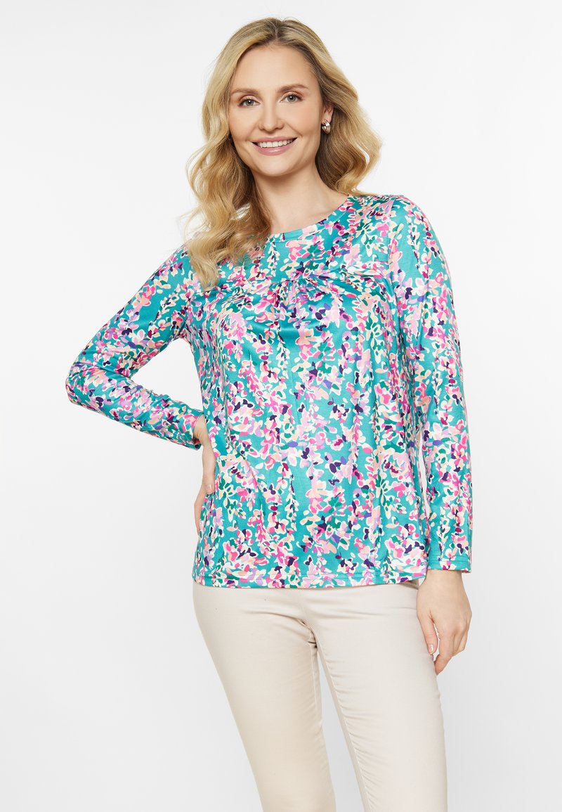 Langærmet, turkis bluse med blomsterprint i pink, lilla og grøn. Har en samlet detalje ved halsen. Glat tekstur.