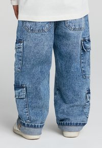 Niebieskie dżinsowe spodnie cargo o luźnym kroju, z wieloma bocznymi kieszeniami i mankietami, z wyblakłym praniem i kontrastowymi szwami.