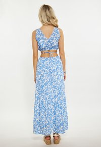 Modrý květinový crop top v kombinaci s odpovídající maxi sukní, s vřetenním výstřihem, s detaily na zavazování a vrstevnatým lemem. Hladká, lehká tkanina.