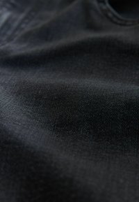 Juodas džinsinis audinys su lygiu paviršiumi, kuriame matyti smulkios pynės bei subtilūs spalvų ir blizgesio atspalviai.