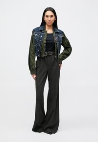 Denim and olive green bomber jacket with a cropped design, paired with black, wide-leg striped pants and a black top. Features metallic accents.