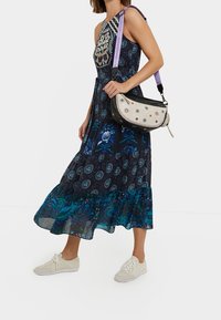 Schwarz mit floralem Muster, blauen Akzenten, gerafftem Saum und einer cremefarbenen Umhängetasche mit bestickten Details und einem dekorativen Gurt.