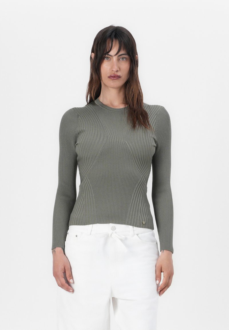 Maglietta a maniche lunghe verde oliva a costine con un design aderente, caratterizzata da dettagli di cucitura sottili e un collo rotondo, abbinata a pantaloni bianchi.
