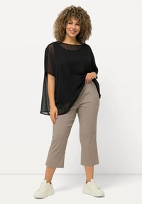 Top nero trasparente con maniche a pipistrello, abbinato a pantaloni cropped beige chiaro e sneaker bianche. Tessuto semplice, design rilassato e senza motivi visibili.
