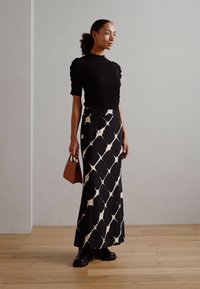 Black textured top with puff sleeves paired with a patterned long skirt in black and cream, complemented by a brown handbag and black boots.